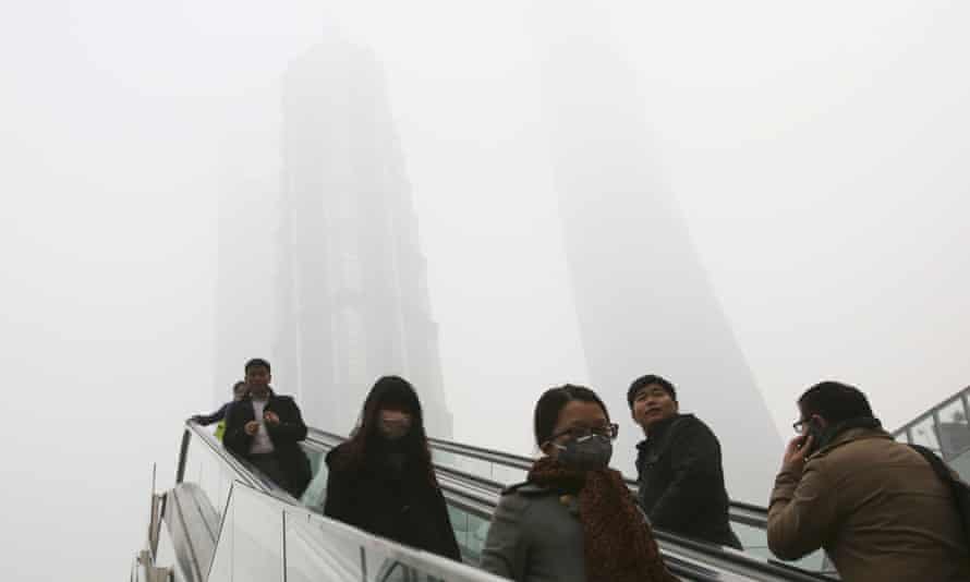 People use escalators with skyscrapers, covered with haze in the background, in Shanghai, China,