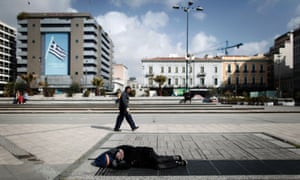 A pedestrian walks past a homeless man sleeping on an air vent above an underground station in Omonia Square in Athens, Greece