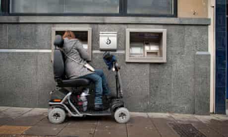 A woman in a powered wheelchair uses a cash machine, UK