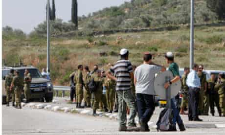 Jewish settler youths look at Israeli security forces