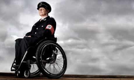 Liz Crow in a wheelchair wearing a Nazi uniform