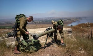 Israeli soldiers cover a rocket at the border with Syria on the Golan Heights as smoke rises from three mortar shells fired as part of the battle in the nearby Syrian village of Al-Madriya.