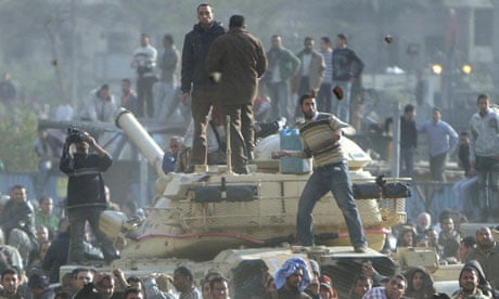 Stone-throwing protesters standing on a tank in Cairo.