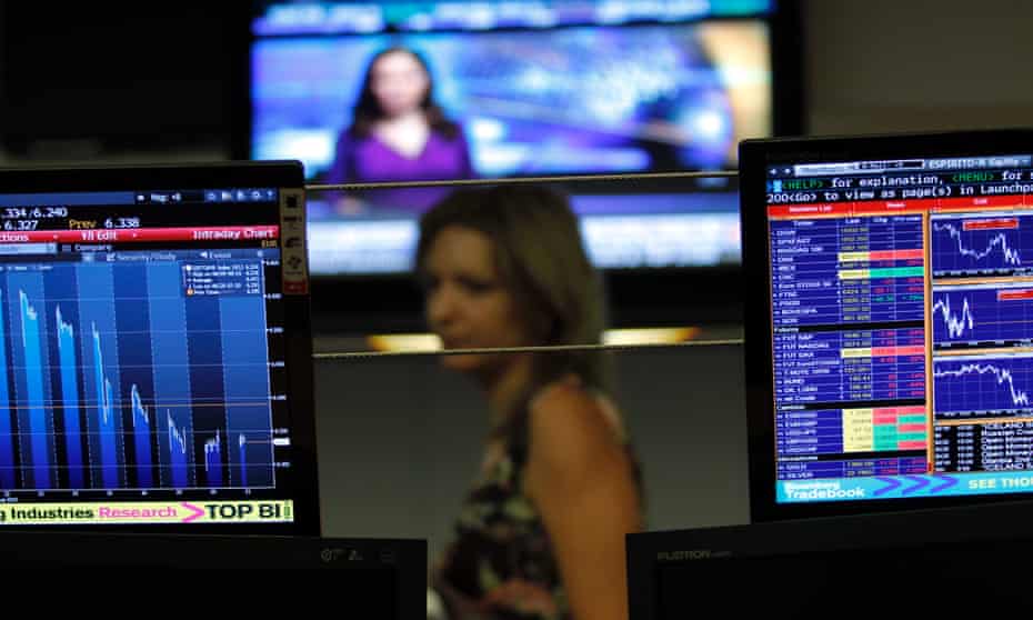 A broker walks behind screens displaying charts  in a trading room of a Portuguese bank.