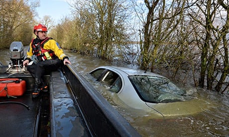 A policeman on a boat looks at a car submerged in floodwater