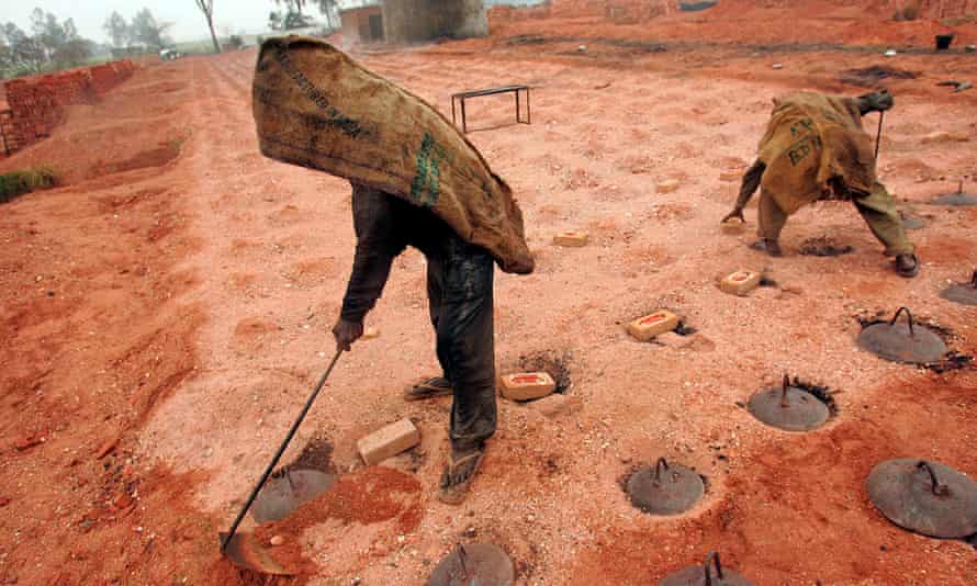 Workers stand on the kilns after closing the opening of a brick kiln and throwing firewood inside.