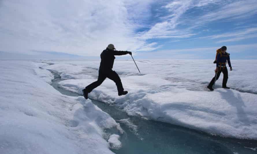 Scientist Ian Joughin of the University of Washington leaps over a small meltwater stream as he walks with Graduate Student, Laura Stevens, from the Massachusetts Institute of Technology and Woods Hole Oceanographic Institution as they conduct research on July 16, 2013 on the Glacial Ice Sheet, Greenland.