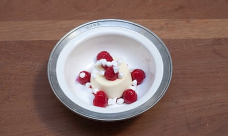 A round lemon mousse with five raspberries around it and one on top