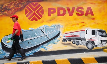A worker walks past a mural with a PDVSA logo at a petrol station in Caracas