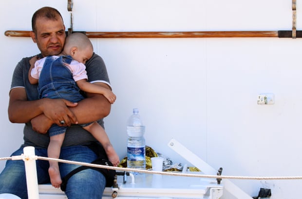 A migrant holds a child before disembarking a coast guard ship in Augusta, Sicily
