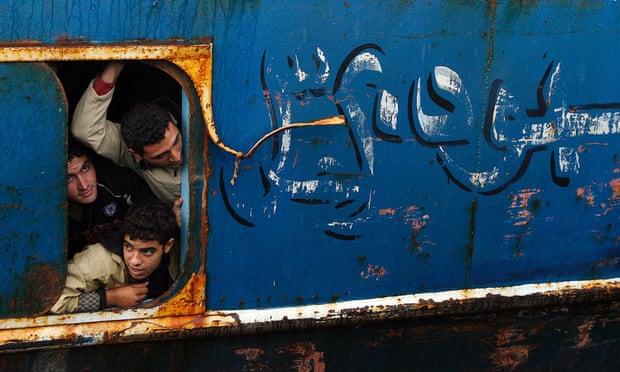 Would-be immigrants look out of a window from a fishing ship as they arrive at Catania harbour