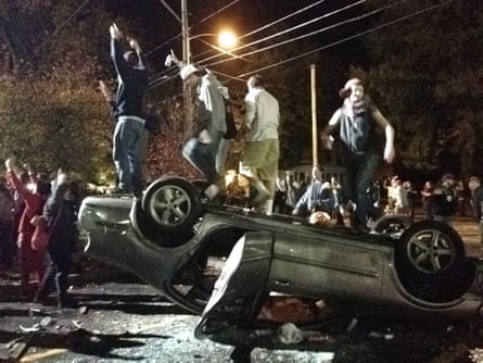 People stand atop an overturned car in Keene, N.H. on Saturday, Oct. 18, 2014, during a night of violent parties that led to destruction, dozens of arrests and multiple injuries, near the city's annual pumpkin festival.  The parties around the school coincided with the annual Keene Pumpkin Festival, where the community tries to set a world record of the largest number of carved and lighted jack-o-lanterns in one place.