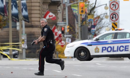 A police officer runs with his weapon drawn outside Parliament Hill in Ottawa.