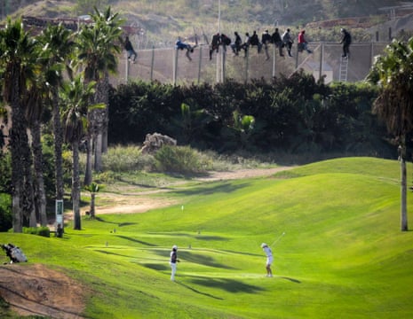 A golfer tees off as African migrants sit on top of a fence during an attempt to enter Spanish territories from Morocco