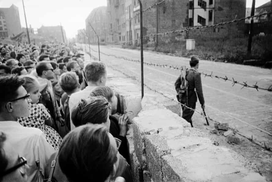 August 1961: A crowd of West Berliners gather at the wall while an East German soldier patrols on the other side.