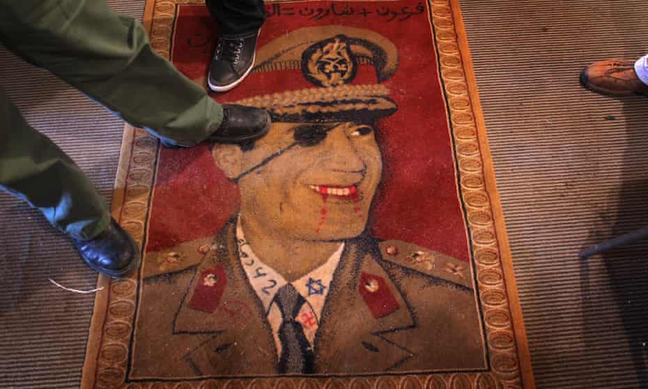 Libyans step on a carpet featuring Libyan leader Muammar Gaddafi on February 25, 2011 in Benghazi, Libya. Gaddafi was killed in October 2011.