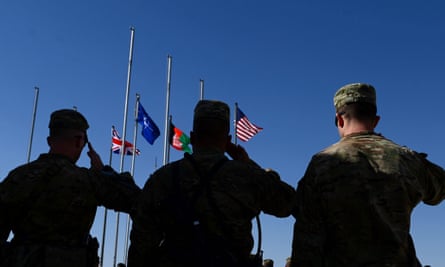 Soldiers salute as the British, Nato, Afghan and US flags are seen on their masts during a handover ceremony before the British and US military withdrawal from Camp Bastion.