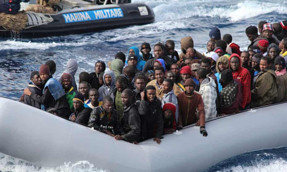Migrants sit in a boat off the coast of Sicily during a mission by the Italian navy as part of its M