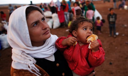 A Syrian Kurdish refugee woman with her daughter wait for transportation after crossing into Turkey.