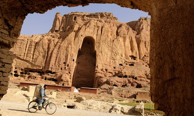 An Afghan man rids his bicycle in front of the empty seat of the Buddha destroyed by the Taliban.
