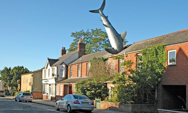 Model of a great white shark stuck head first into the roof of a house