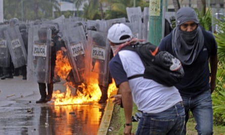 Riot police stamp out flames after a fire bomb was thrown at them during violent protests in Acapulco.