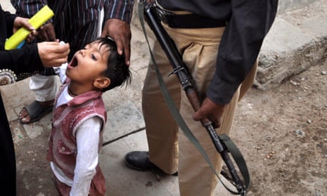 A policeman escorts a Pakistani health worker as she administers the polio vaccine in Karachi