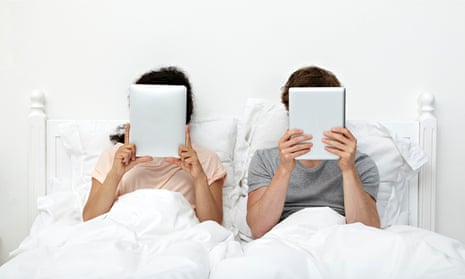 Couple looking at digital tablets in bed