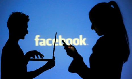 People pose with laptops in front of projection of Facebook logo in this picture illustration