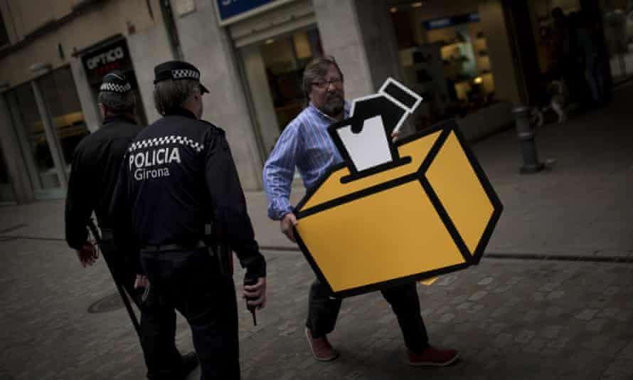 Businessman Emilio Busquets walks past two police officers patrolling the street, as he holds a drawing of a ballot box to decorate his shop.