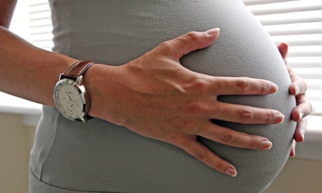 Woman's hands with wristwatch on pregnant belly 