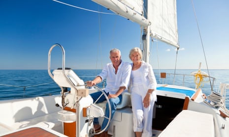 DE3TRN A happy senior couple sitting at the wheel of a sail boat on a calm blue