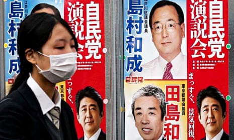 A woman passes election posters in Tokyo, with the prime minister, Shinzo Abe, bottom right. Only 12