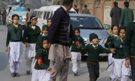A plainclothes security officer escorts students rescued an army school during a Taliban attack in Peshawar, Pakistan