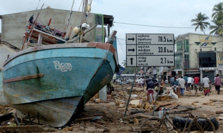 Sri Lankan residents walk past a fishing boat marooned on a road after a massive tidal wave struck the southern district of Galle, taken on 27 December 2004
