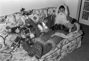 Arsenal and England footballer Kenny Sansom dressed up as Father Christmas as he relaxes on his present laden sofa in 1982
