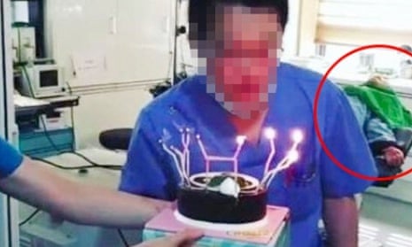A member of staff blows out a birthday cake with an unconscious patient on the operating table behind him