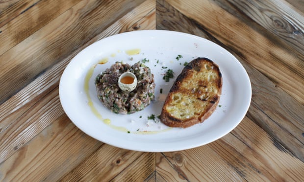 A round of fallow buck haunch steak tartare with a quail's egg in the middle and a chunk of fire-toasted bread, served on a white plate