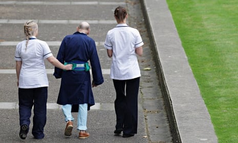 Two NHS staff walk with an elderly patient 