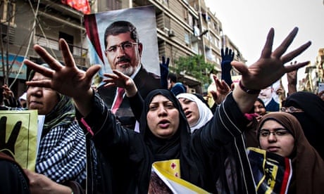 A woman stretches out her hands towards the camera in front of a poster of Morsi in street in Cairo