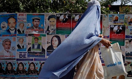 An Afghan woman walks past by election posters of parliamentary candidates in Jalalabad, Afghanistan