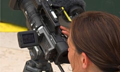Woman videographer filming for BBC television checking LCD monitor on camera