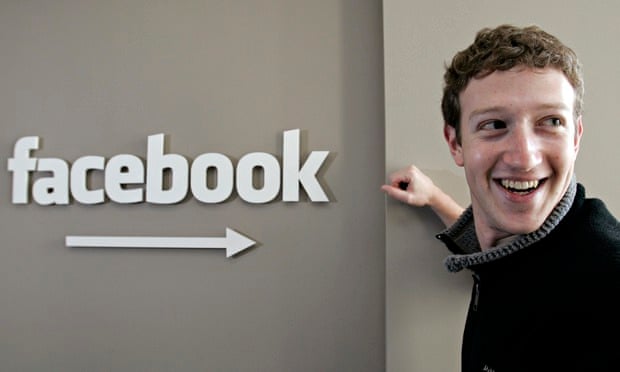 Mark Zuckerberg CEO of Facebook stands next to a Facebook sign smiling
