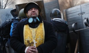 A priest stands next to protesters at a barricade.