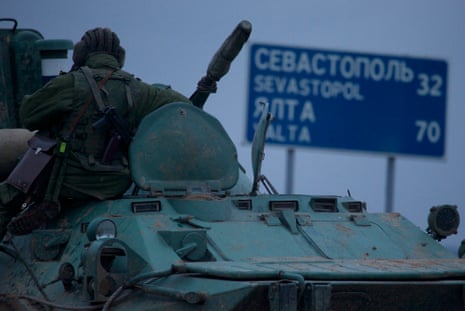 A soldier rests atop a Russian armored personnel carriers with a road sign reading "Sevastopol - 32 kilometers, Yalta - 70 kilometers", near the town of Bakhchisarai, Ukraine, Friday, Feb. 28, 2014.