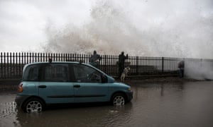 People take photographs as waves crash against the seafront at Dawlish.