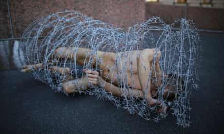 Pyotr Pavlensky lies on the ground, wrapped in barbed wire roll