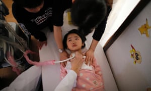 A doctor conducts a thyroid examination on five-year-old girl as her older brother and a nurse take care of her at a clinic in temporary housing complex in Nihonmatsu.