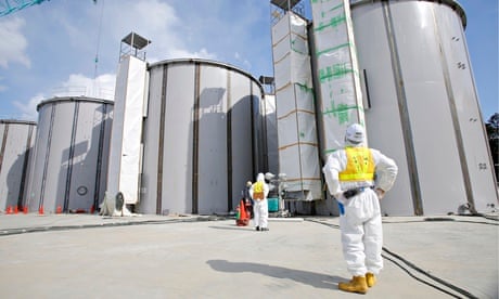 A worker in a protective suit looks at tanks, under construction, to store radioactive water