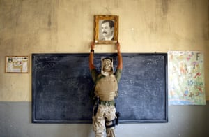 A US Marine pulls down a picture of Saddam Hussein at a school on April 16, 2003 in Kut, Iraq. A combination team from the marines, army and special forces went to schools and other facilities in Kut, looking for weapons and unexploded bombs in preparation for removing and neutralising them.